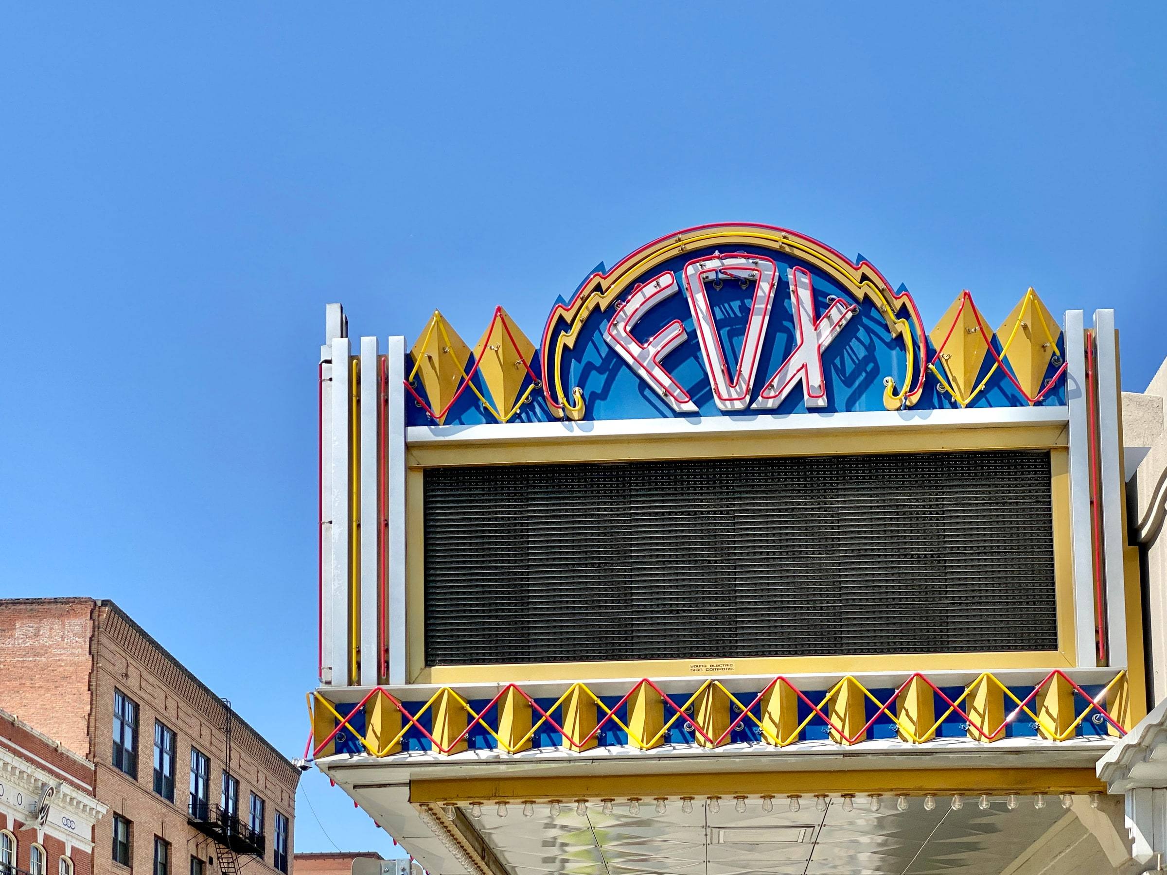 The neon marquee of the Fox Theater in Spokane, Washington, its yellow and blue art deco sign glowing against a clear sky above a blank black letter board.