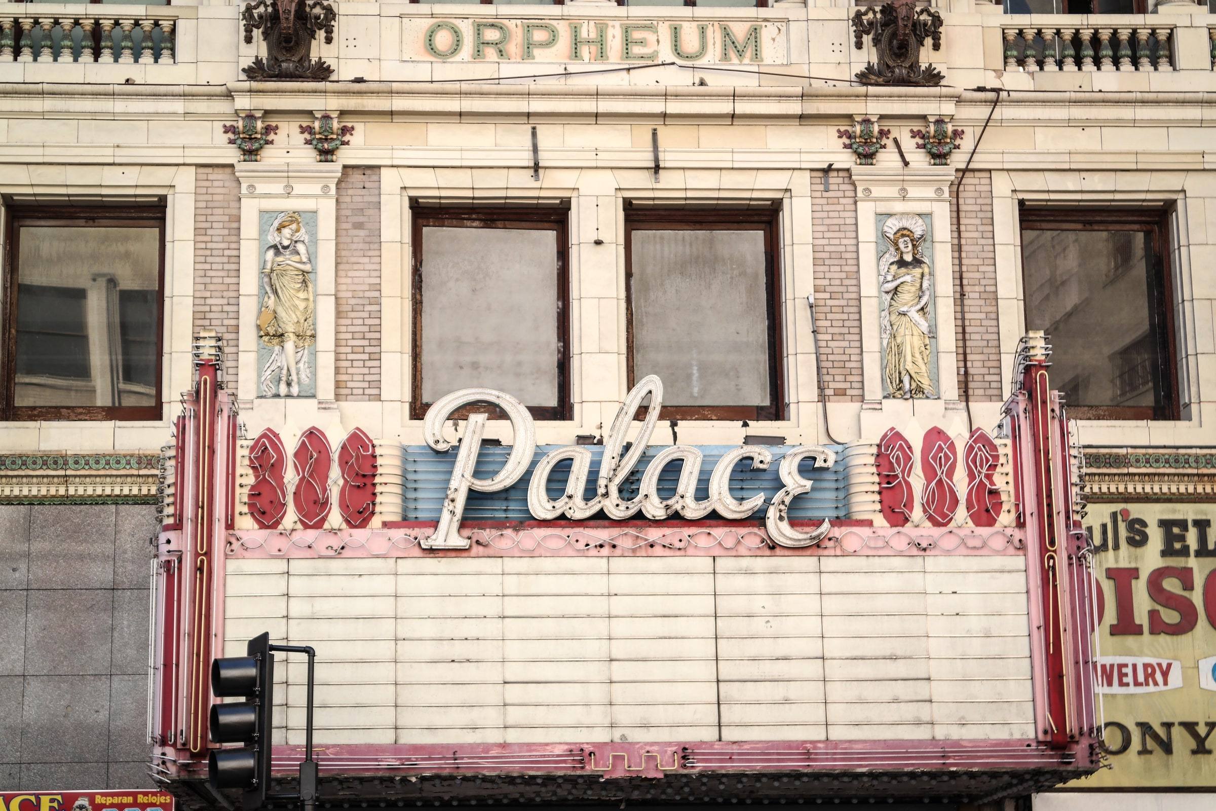 The ornate, weathered facade of a historic theater with a vintage neon 'Palace' marquee whose letter board is blank, below carved stonework and arched windows.