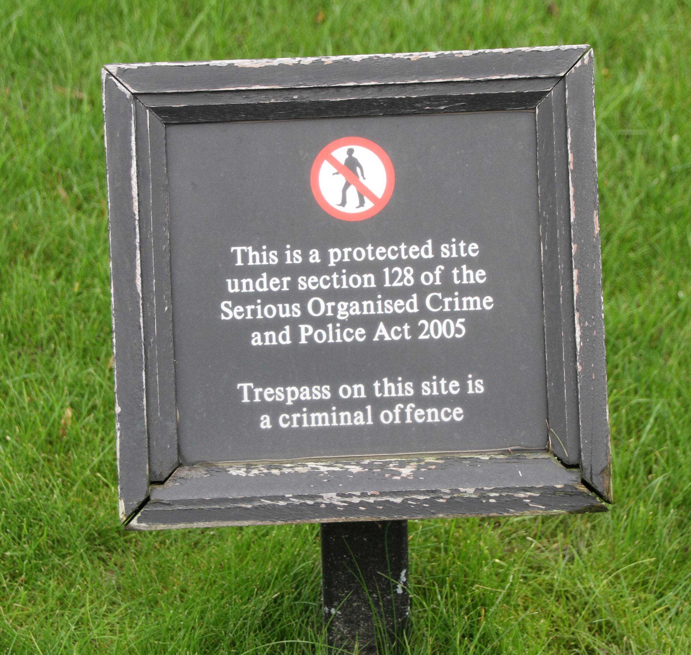 A small black sign on a lawn warning that the site is protected and that trespass on it is a criminal offence.