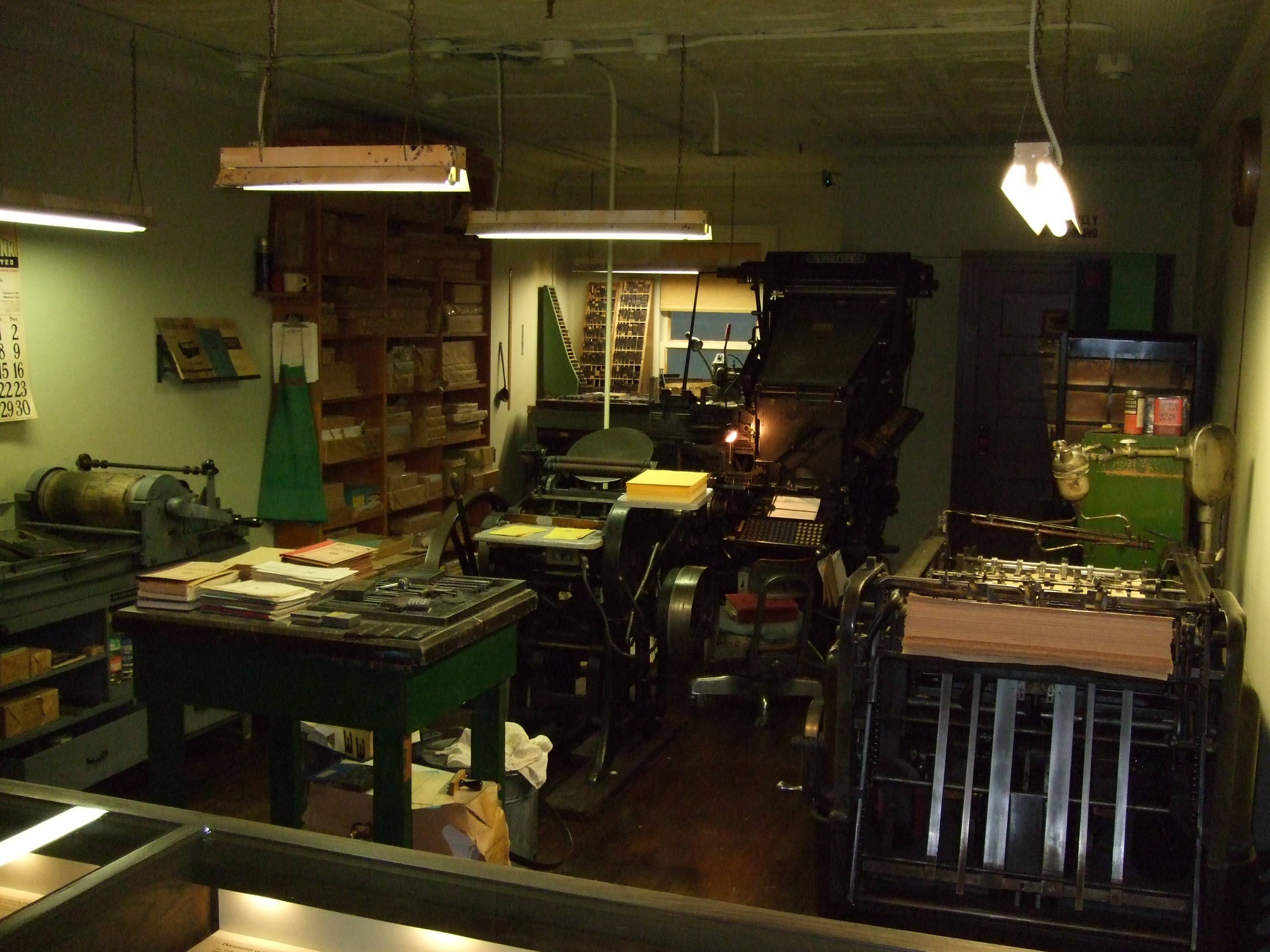 An old print shop with vintage letterpress machines, type cases and hanging lamps, empty of people