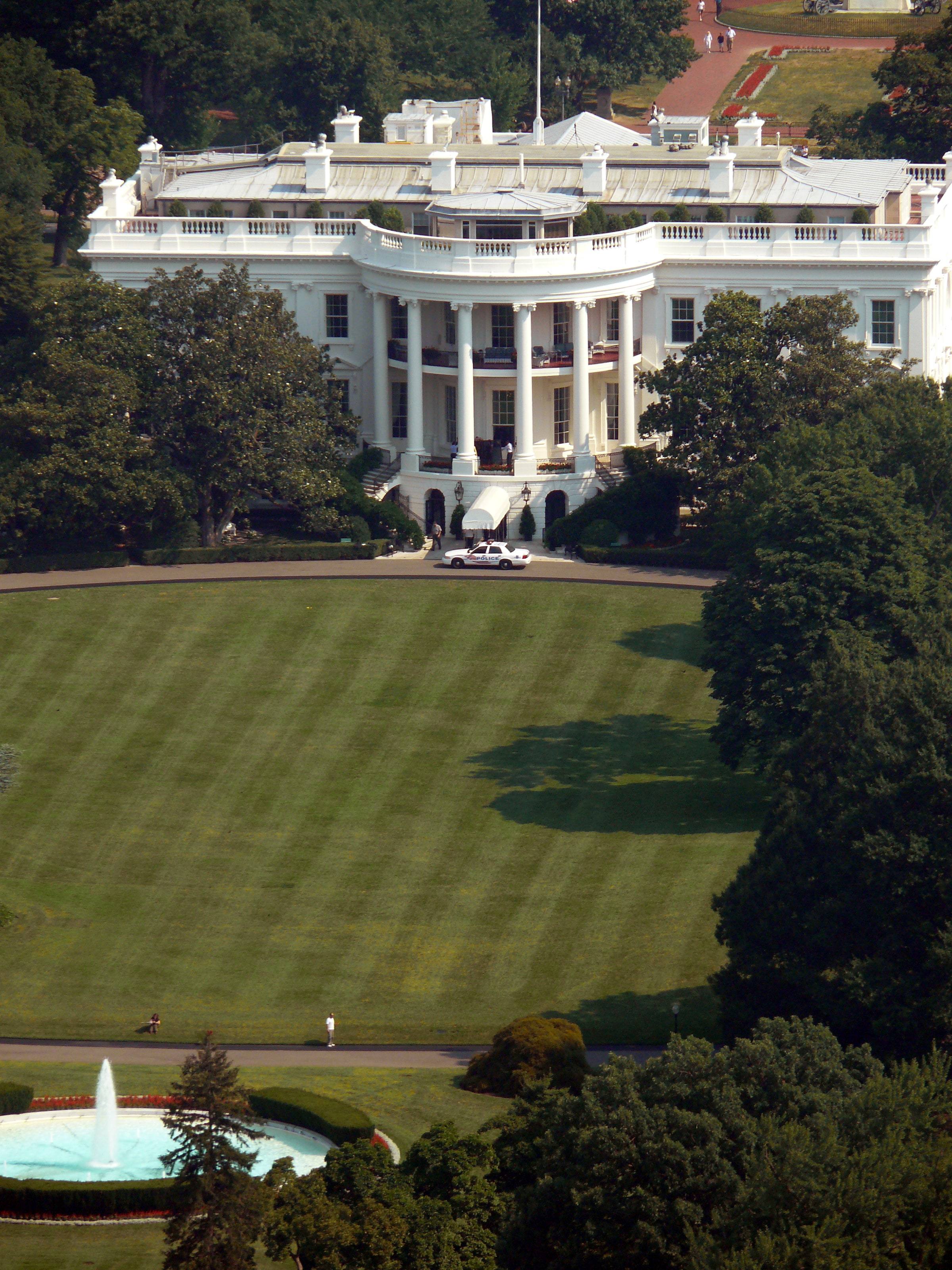 The south facade of the White House and the South Lawn, seen from a distance, with the fountain in the foreground and trees framing the grounds.